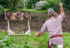 A man throwing a tomahawk outside at three tartgets