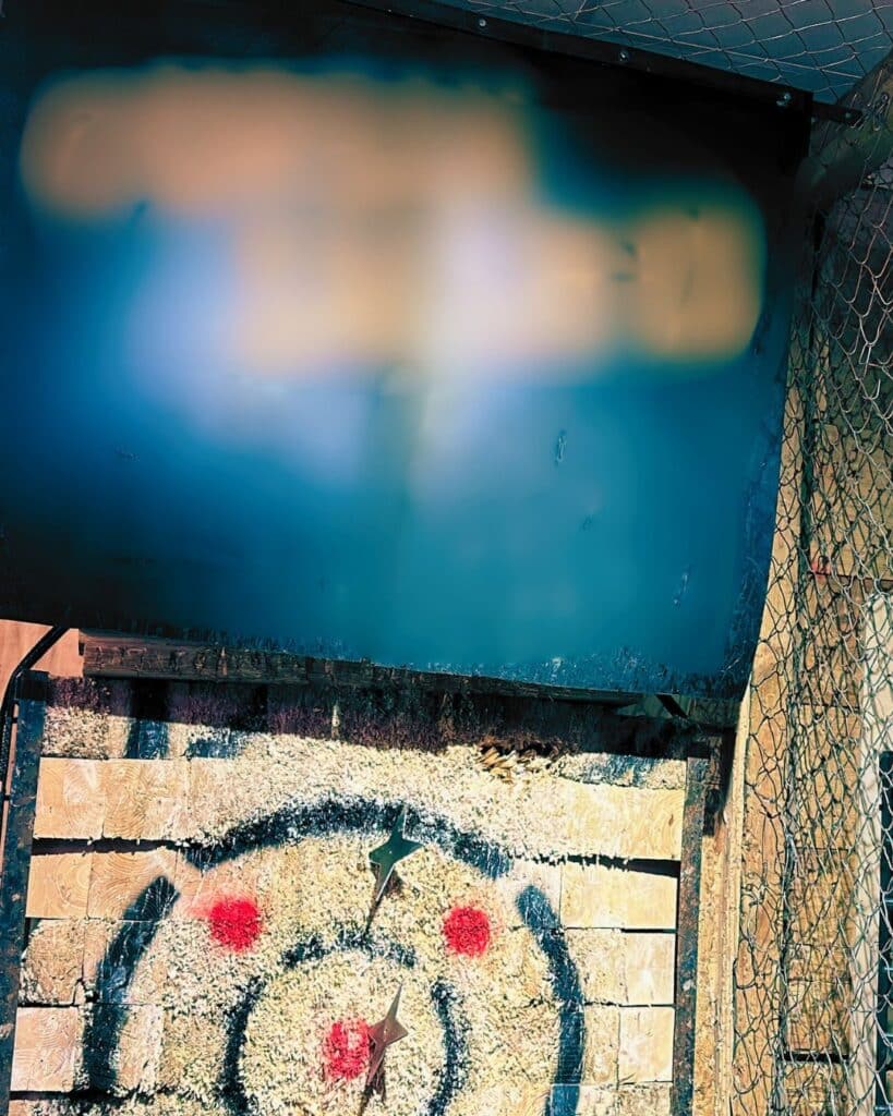 An axe throwing target with a rubber horse mat suspended above it for safety