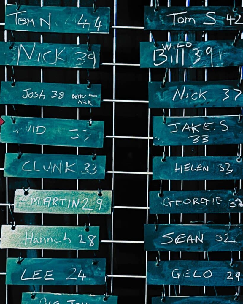 A leaderboard made up of multiple small chalkboards with named and scores on mounted on a metal grid