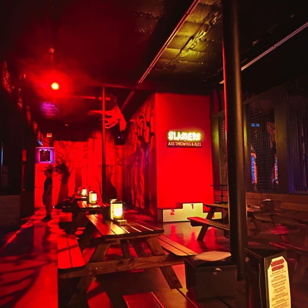 Inside of Slasher axe throwing bar with lots of red light, black background and horror themed props
