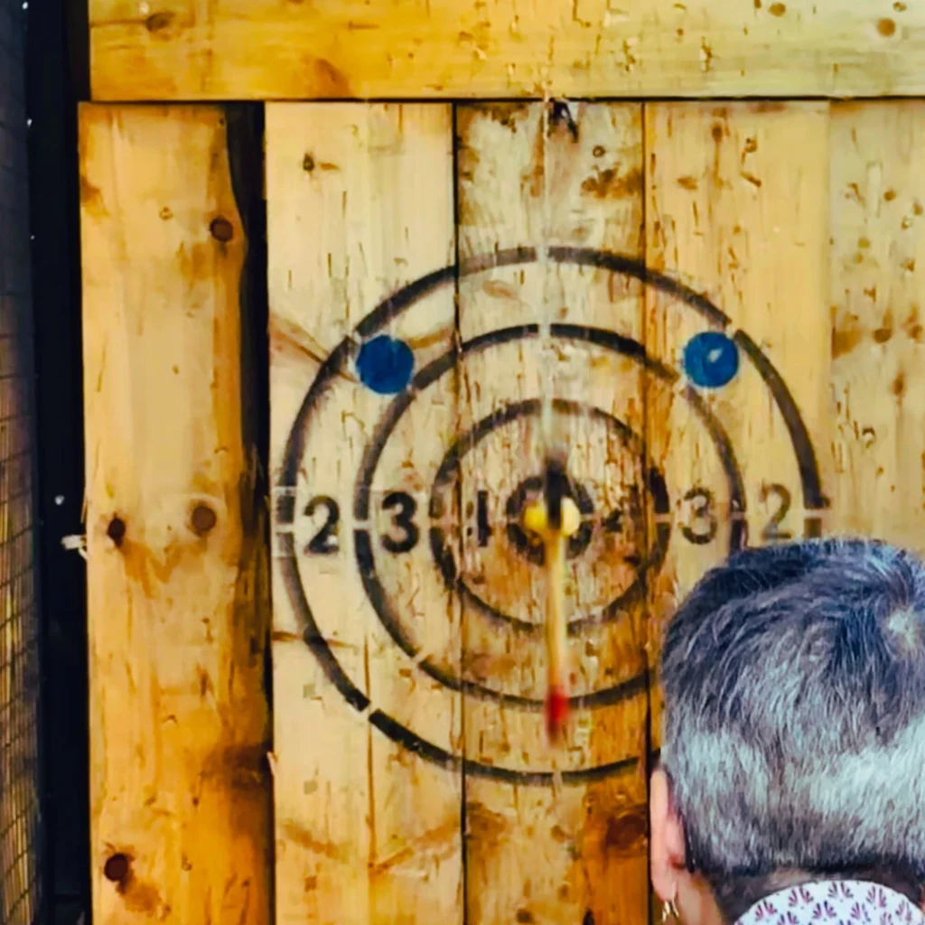 An axe hitting an apple hanging in front of an axe throwing board